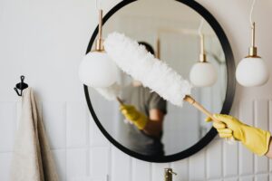 Peerless - Person dusting mirror in home.