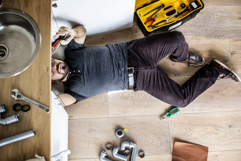 man working on pipes under kitchen sink